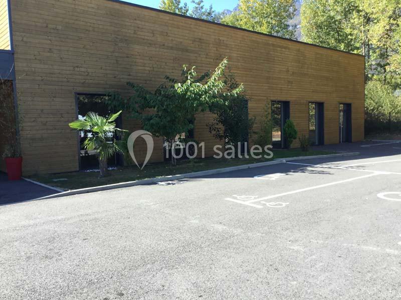 Façade en bois d'un bâtiment moderne avec des arbres et des plantes devant, bordée par un parking vide.