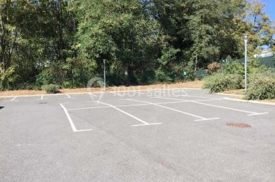 Parking vide avec marquages au sol, situé devant un bâtiment en bois entouré d'arbres et de montagnes.