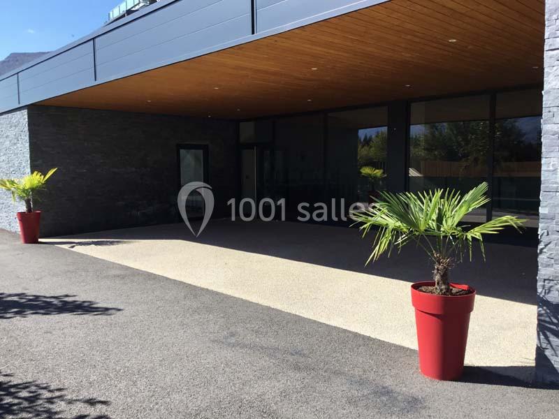Entrée d'un bâtiment moderne avec façade en verre, toit en bois et deux plantes en pot rouge sur le devant.