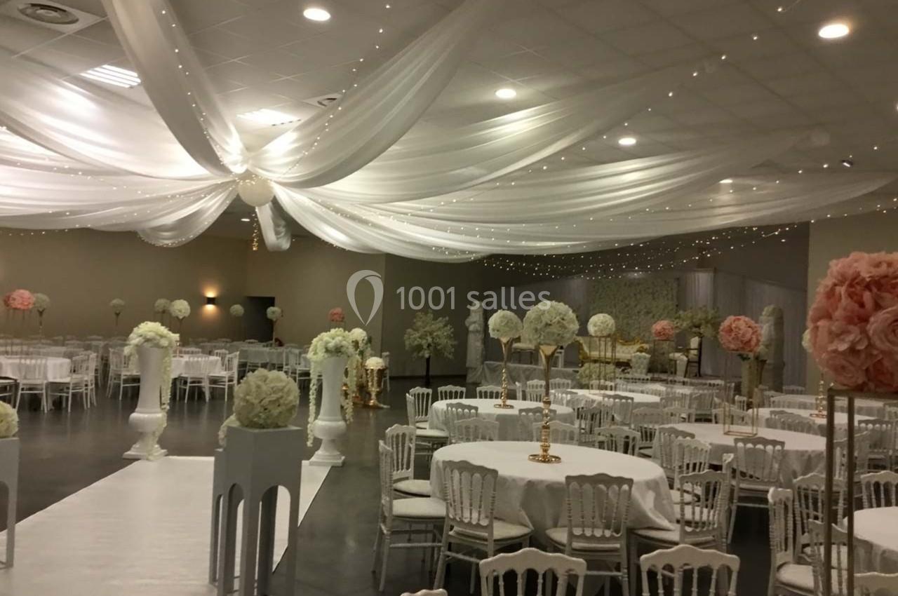 Salle de réception décorée avec des tables rondes, des chaises blanches et des drapés blancs suspendus au plafond.