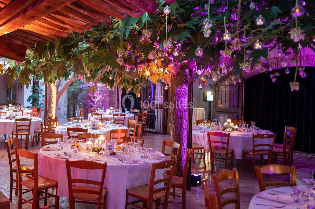 Salle de réception décorée avec des tables rondes dressées, éclairage tamisé et végétation suspendue.