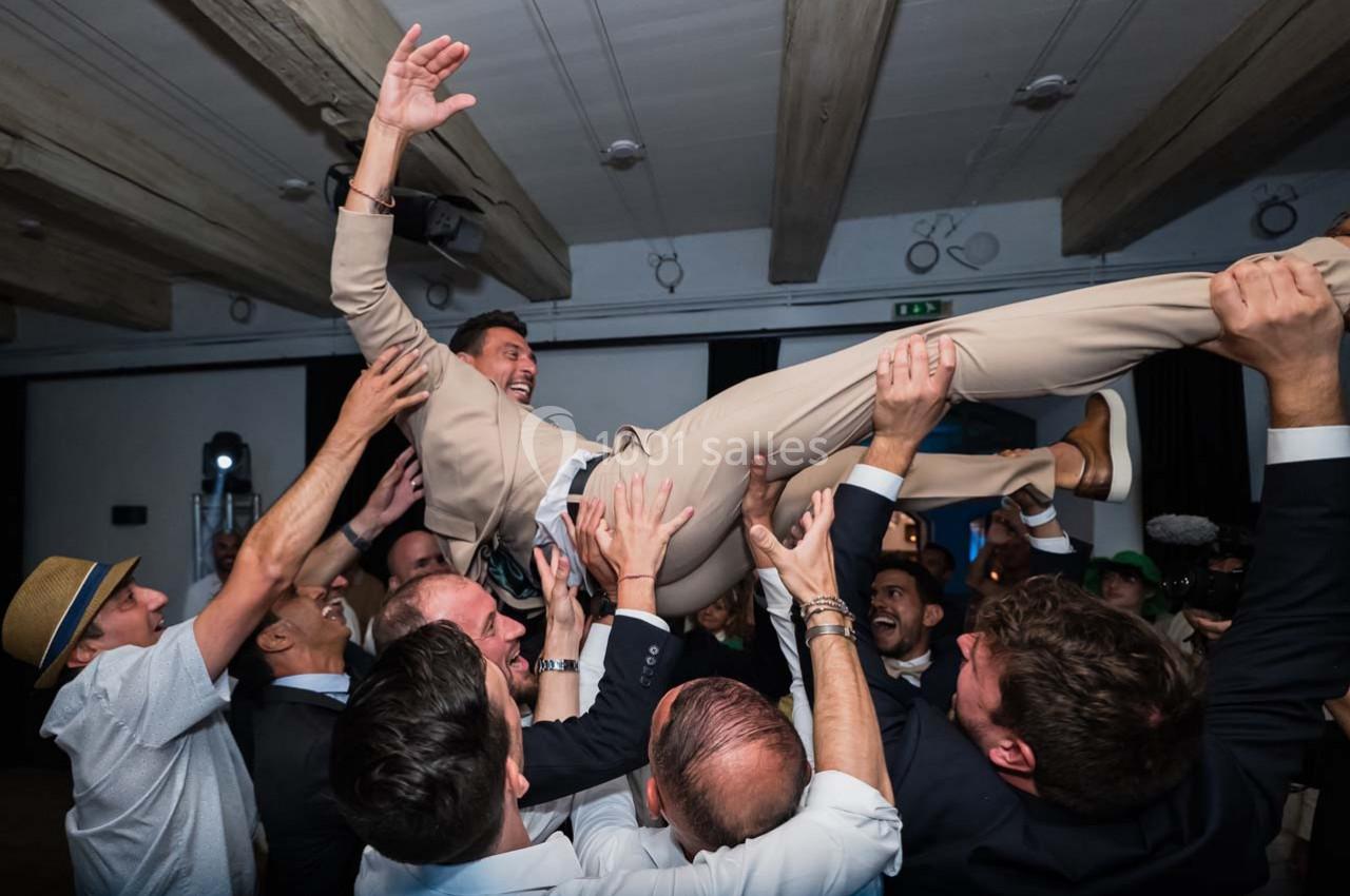 Un groupe d'hommes soulève un homme en costume beige lors d'une célébration dans une salle.