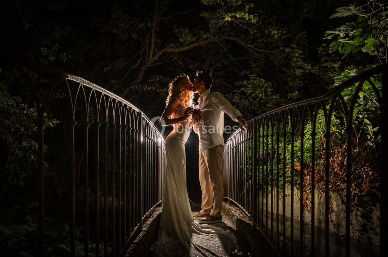 Un couple élégant se tient sur un pont éclairé la nuit, partageant un moment romantique.