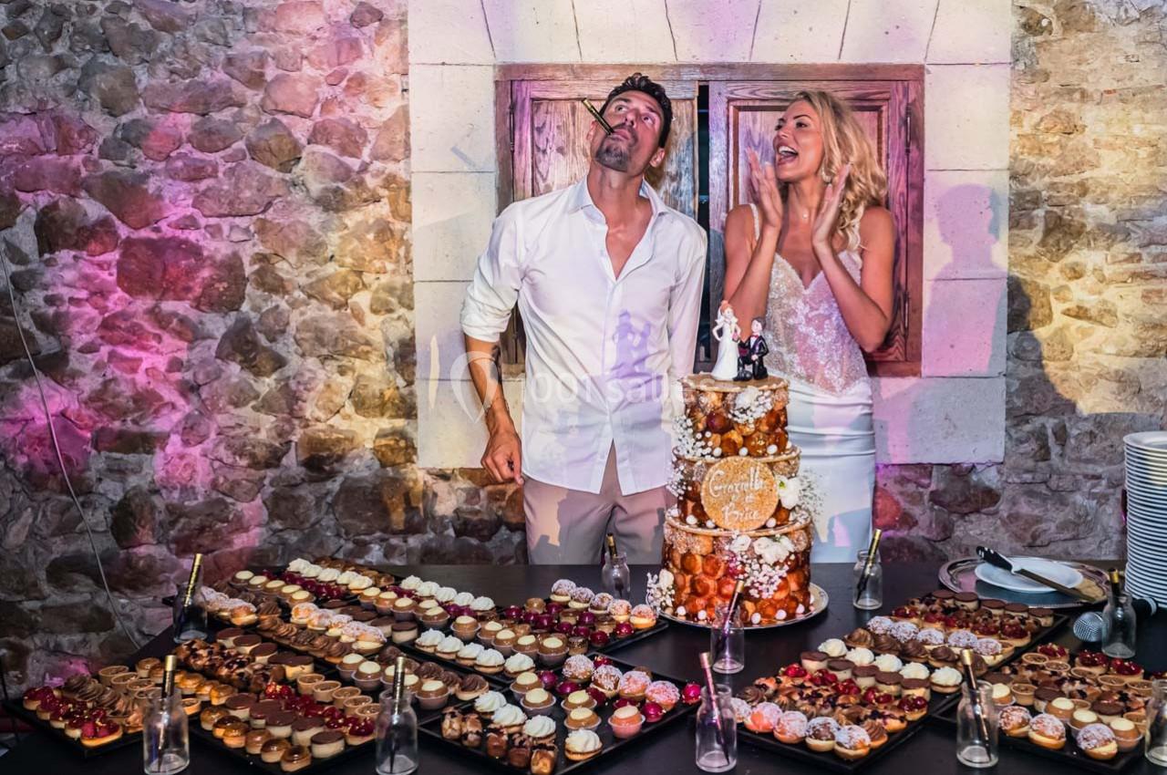 Un couple souriant devant une pièce montée et des plateaux de desserts, dans une salle en pierre éclairée.