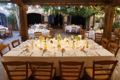 Salle de réception avec tables rondes dressées, nappes blanches, chaises en bois et décoration florale.
