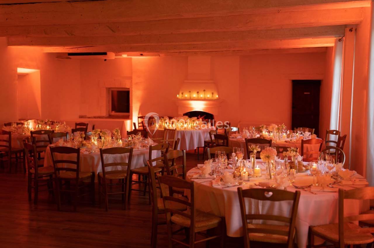 Salle de réception chaleureusement éclairée, avec des tables rondes dressées pour un dîner élégant.