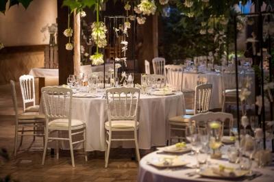 Salle de réception avec tables rondes dressées, nappes blanches, chaises en bois et décoration florale.