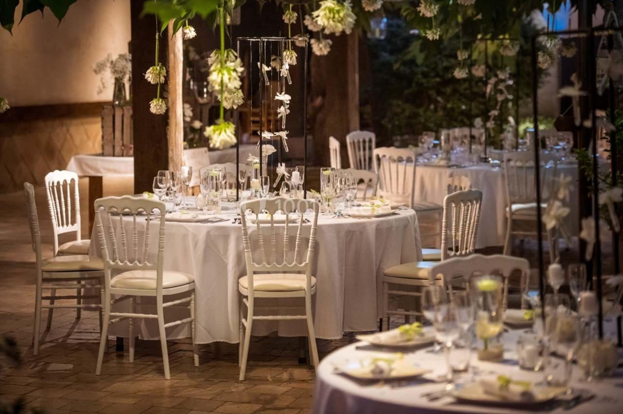 Salle de réception décorée avec des tables rondes, nappes blanches, chaises élégantes et éclairage tamisé.