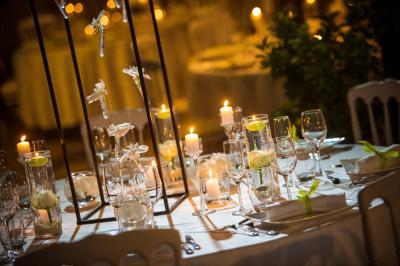 Salle de réception avec tables rondes dressées, nappes blanches, chaises en bois et décoration florale.