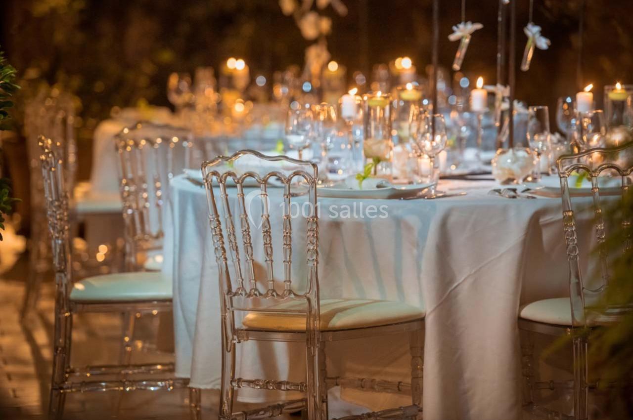 Table élégamment dressée avec nappes blanches, chaises transparentes et bougies allumées dans une ambiance tamisée.