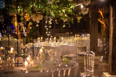 Salle de réception avec tables rondes dressées, nappes blanches, chaises en bois et décoration florale.