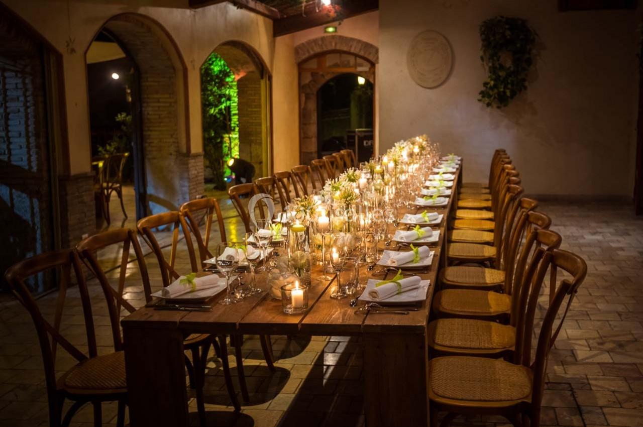Grande table en bois décorée de bougies et de serviettes blanches, entourée de chaises dans une salle éclairée…