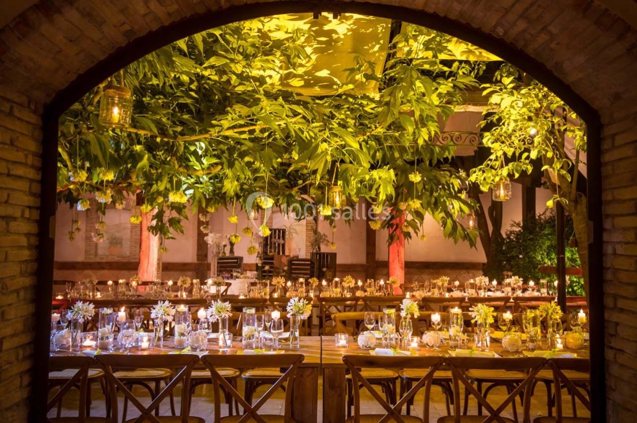 Salle de réception décorée avec des tables en bois, des chandelles et des arbres illuminés créant une ambiance chaleureuse.