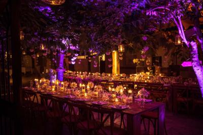 Salle de réception avec tables rondes dressées, nappes blanches, chaises en bois et décoration florale.