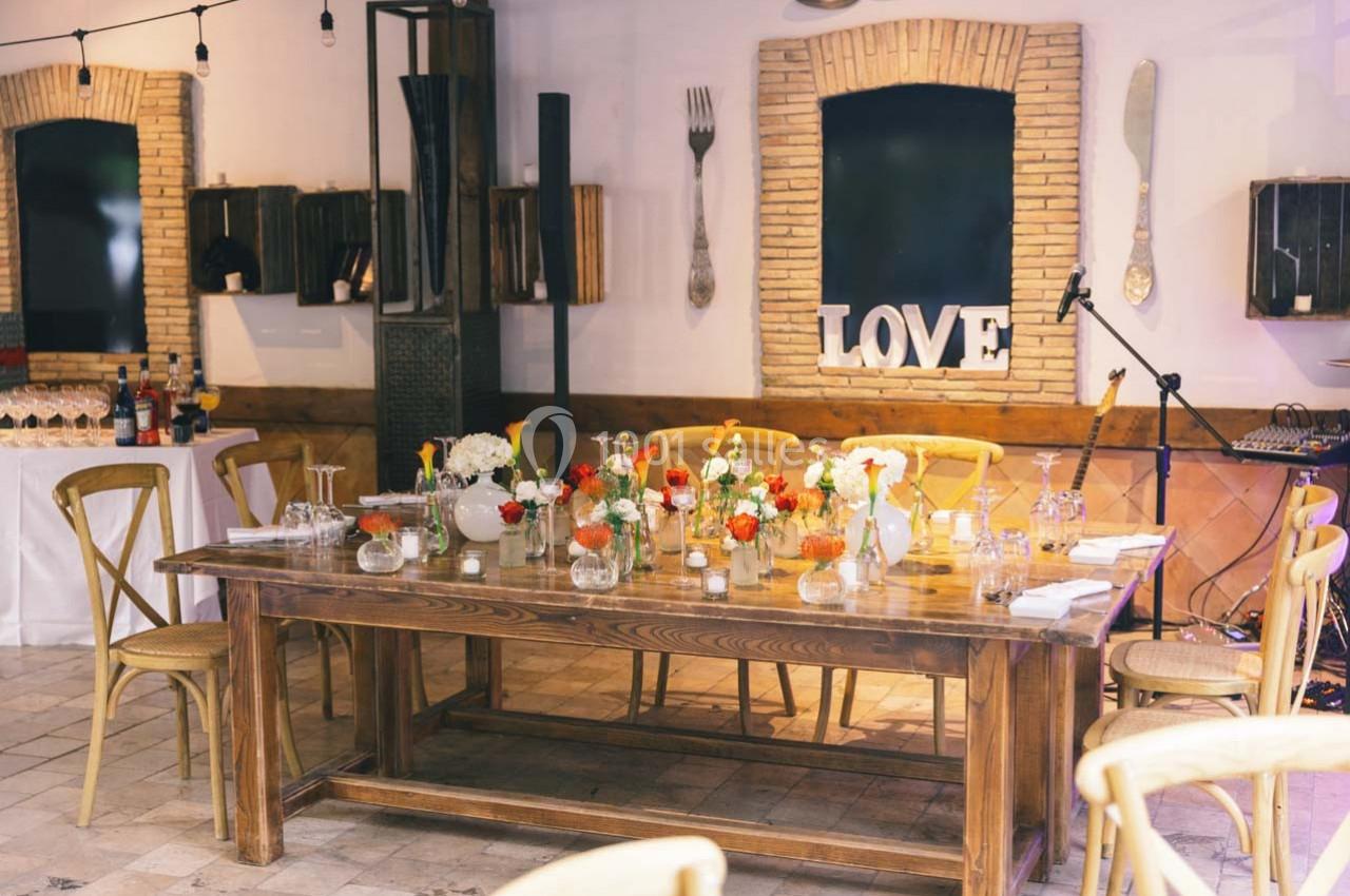 Table en bois décorée de fleurs et bougies dans une salle lumineuse avec des éléments de décoration murale.