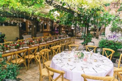 Salle de réception avec tables rondes dressées, nappes blanches, chaises en bois et décoration florale.