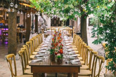 Salle de réception avec tables rondes dressées, nappes blanches, chaises en bois et décoration florale.