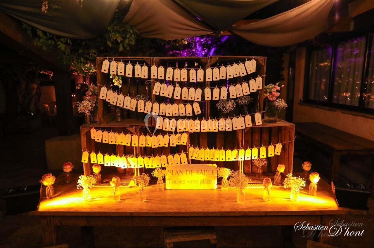 Plan de table lumineux avec étiquettes suspendues, entouré de décorations florales dans une ambiance tamisée.