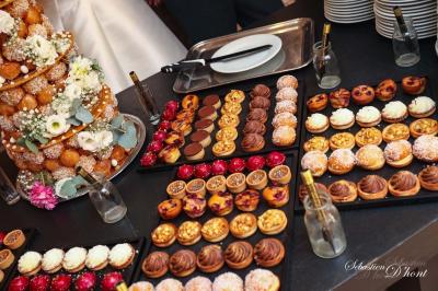 Salle de réception avec tables rondes dressées, nappes blanches, chaises en bois et décoration florale.