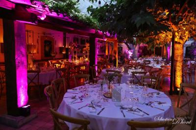 Salle de réception avec tables rondes dressées, nappes blanches, chaises en bois et décoration florale.