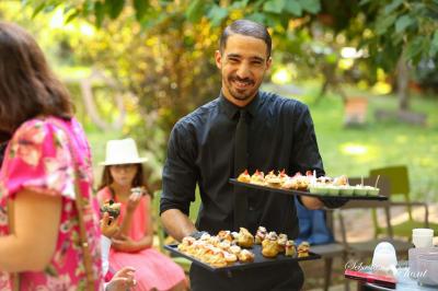 Salle de réception avec tables rondes dressées, nappes blanches, chaises en bois et décoration florale.