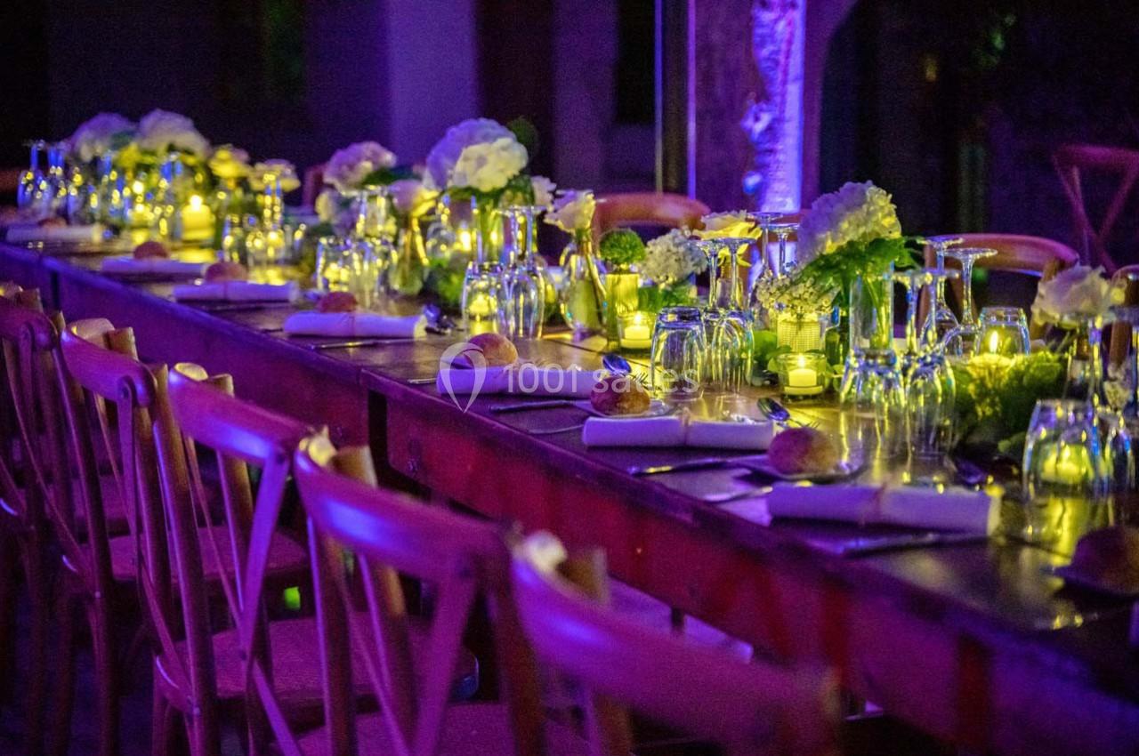 Table décorée avec des fleurs, bougies et vaisselle élégante, éclairée par une lumière tamisée dans une ambiance festive.