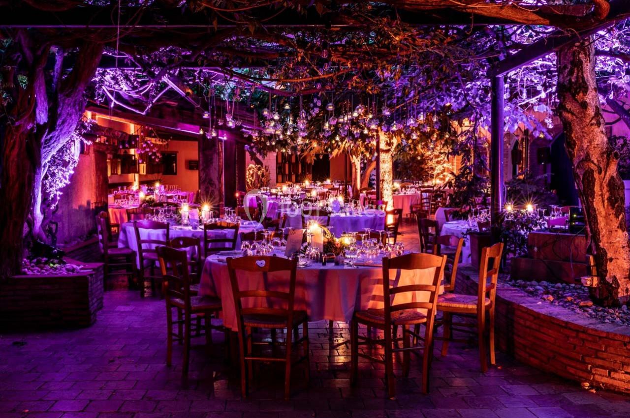 Salle de réception en extérieur décorée de guirlandes lumineuses et tables dressées pour un événement nocturne.