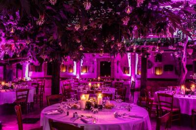 Salle de réception avec tables rondes dressées, nappes blanches, chaises en bois et décoration florale.