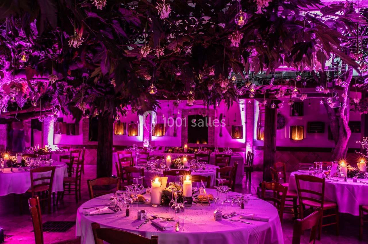 Salle de réception décorée avec des tables rondes, bougies allumées et éclairage rose créant une ambiance festive.