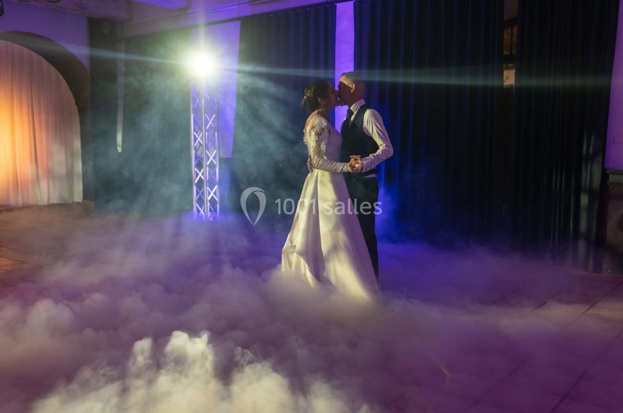 Un couple de mariés danse dans une ambiance éclairée par des projecteurs et entourée de fumée au sol.
