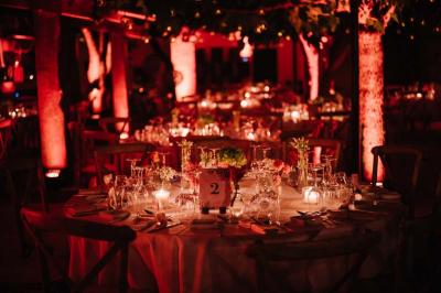 Salle de réception avec tables rondes dressées, nappes blanches, chaises en bois et décoration florale.