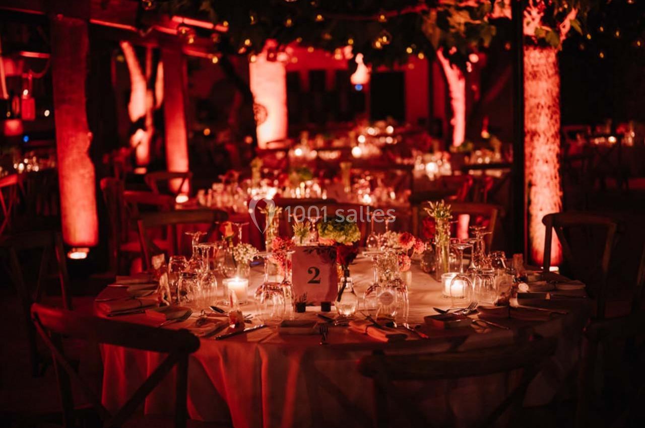 Tables rondes décorées avec des bougies et des fleurs, éclairées par une lumière rouge dans un cadre extérieur nocturne.