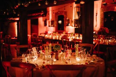 Salle de réception avec tables rondes dressées, nappes blanches, chaises en bois et décoration florale.