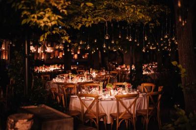 Salle de réception avec tables rondes dressées, nappes blanches, chaises en bois et décoration florale.