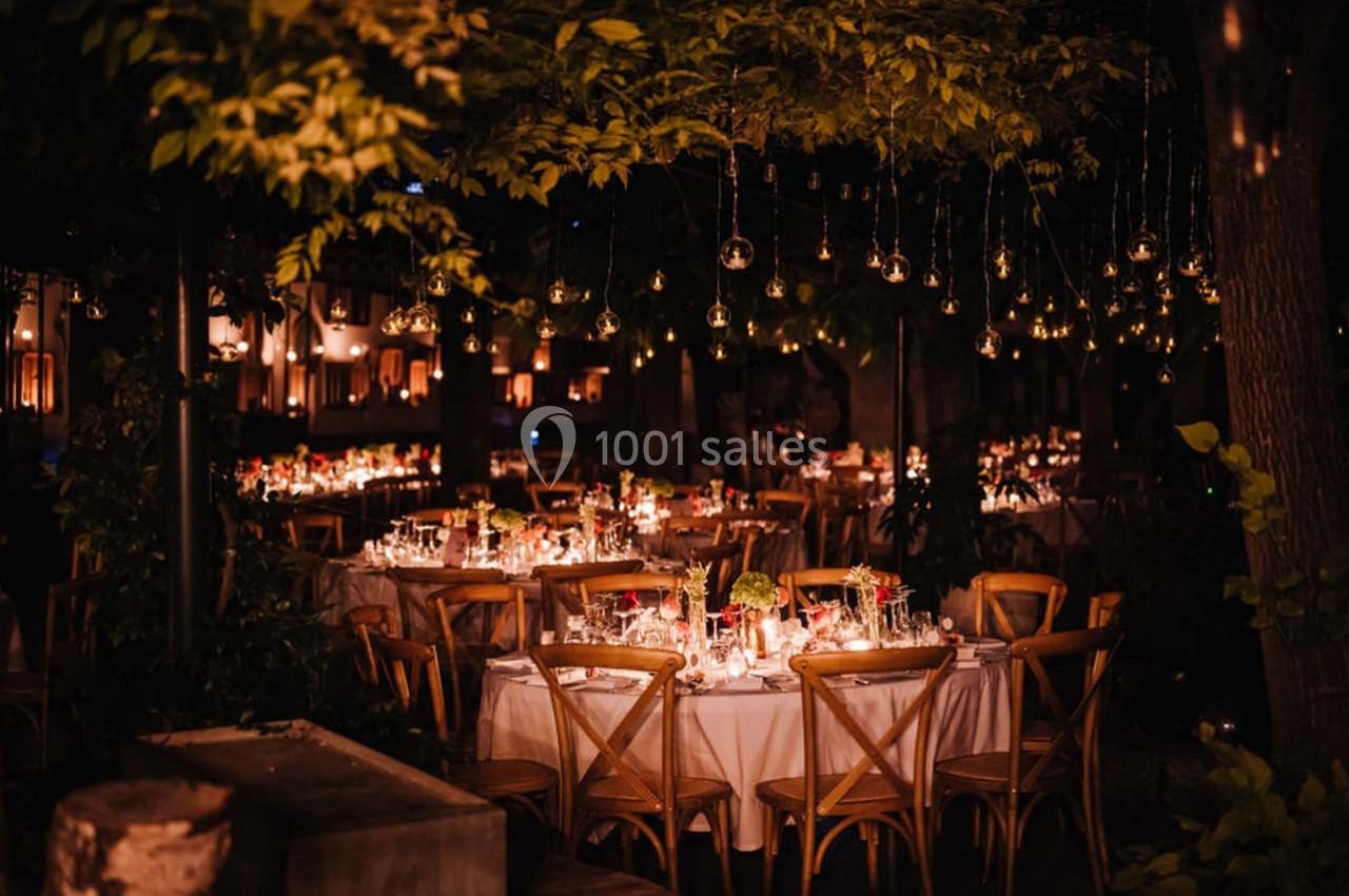 Tables décorées avec des bougies et des fleurs sous des guirlandes lumineuses dans un jardin en soirée.
