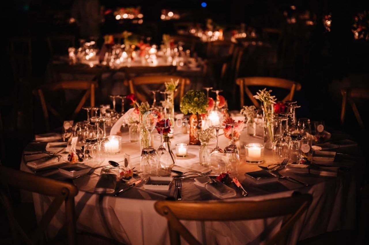 Table élégamment dressée avec des bougies allumées, des fleurs et des verres, dans une ambiance tamisée.