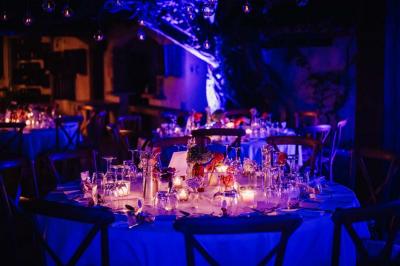 Salle de réception avec tables rondes dressées, nappes blanches, chaises en bois et décoration florale.