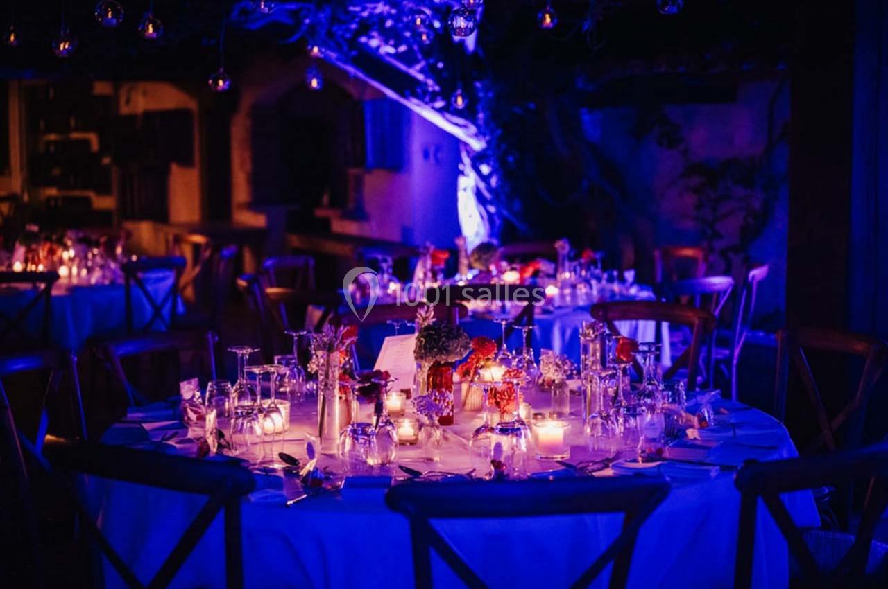 Table ronde décorée pour un dîner, éclairée par des bougies et des lumières violettes dans une ambiance nocturne.