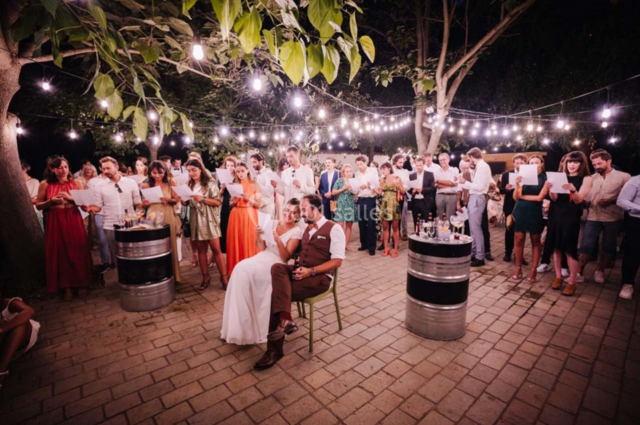 Groupe de personnes rassemblées en soirée extérieure sous des guirlandes lumineuses, certaines tenant des feuilles.