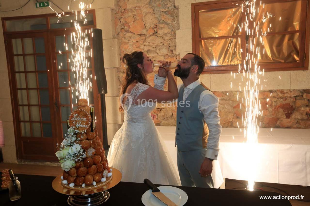 Un couple en tenue de mariage trinque devant une pièce montée, entouré d'étincelles festives.