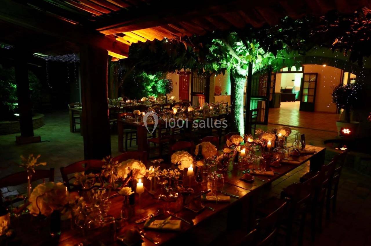 Salle de réception en soirée, éclairée par des lumières chaudes et décorée de tables dressées avec des fleurs et des bougies.