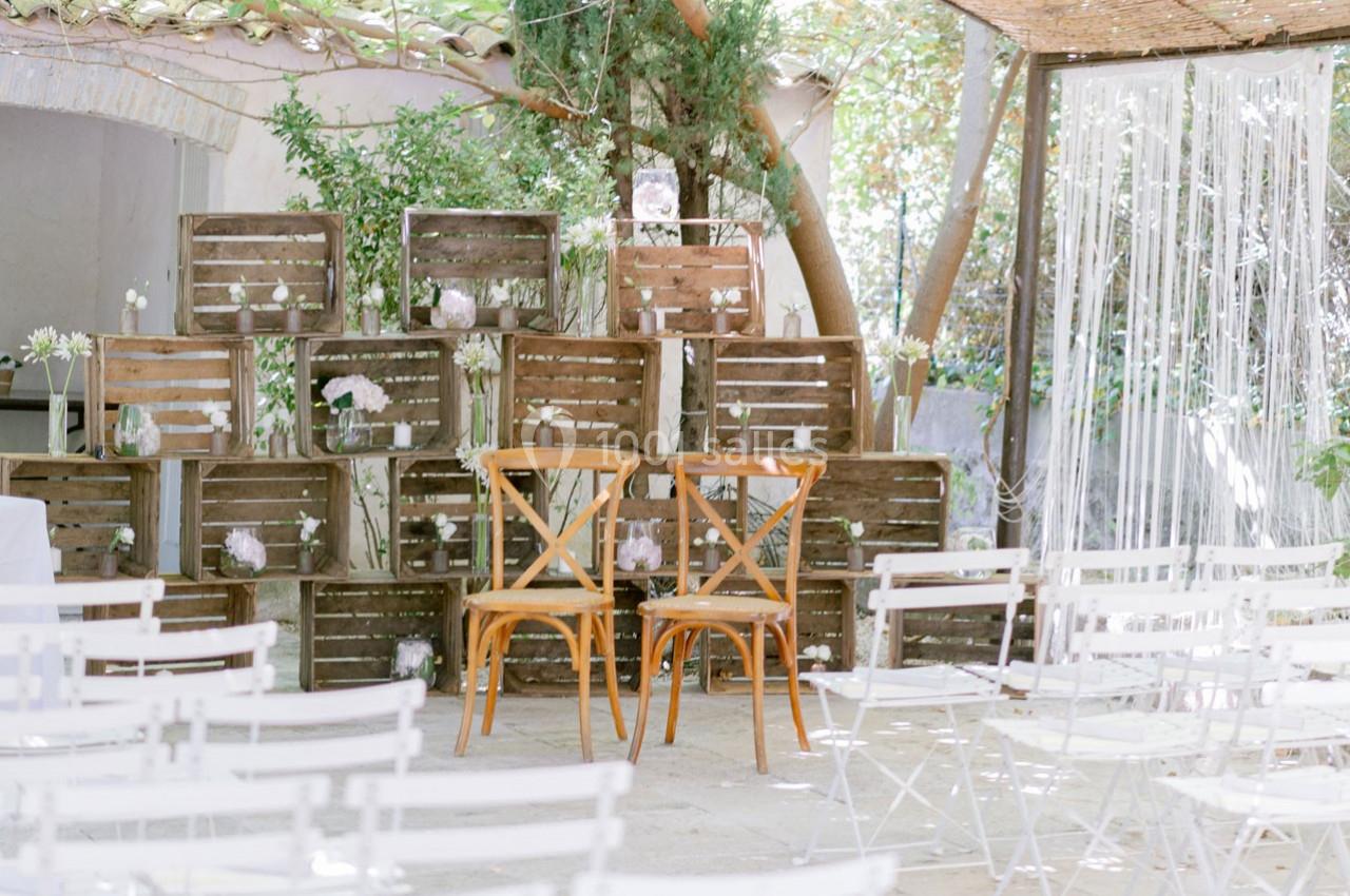 Deux chaises en bois devant un décor rustique composé de caisses en bois et de fleurs, dans un espace extérieur.