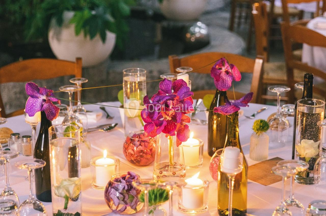 Table décorée avec des fleurs violettes, bougies allumées et verres, dans un cadre extérieur élégant.