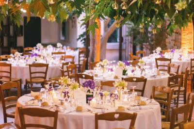 Salle de réception avec tables rondes dressées, nappes blanches, chaises en bois et décoration florale.