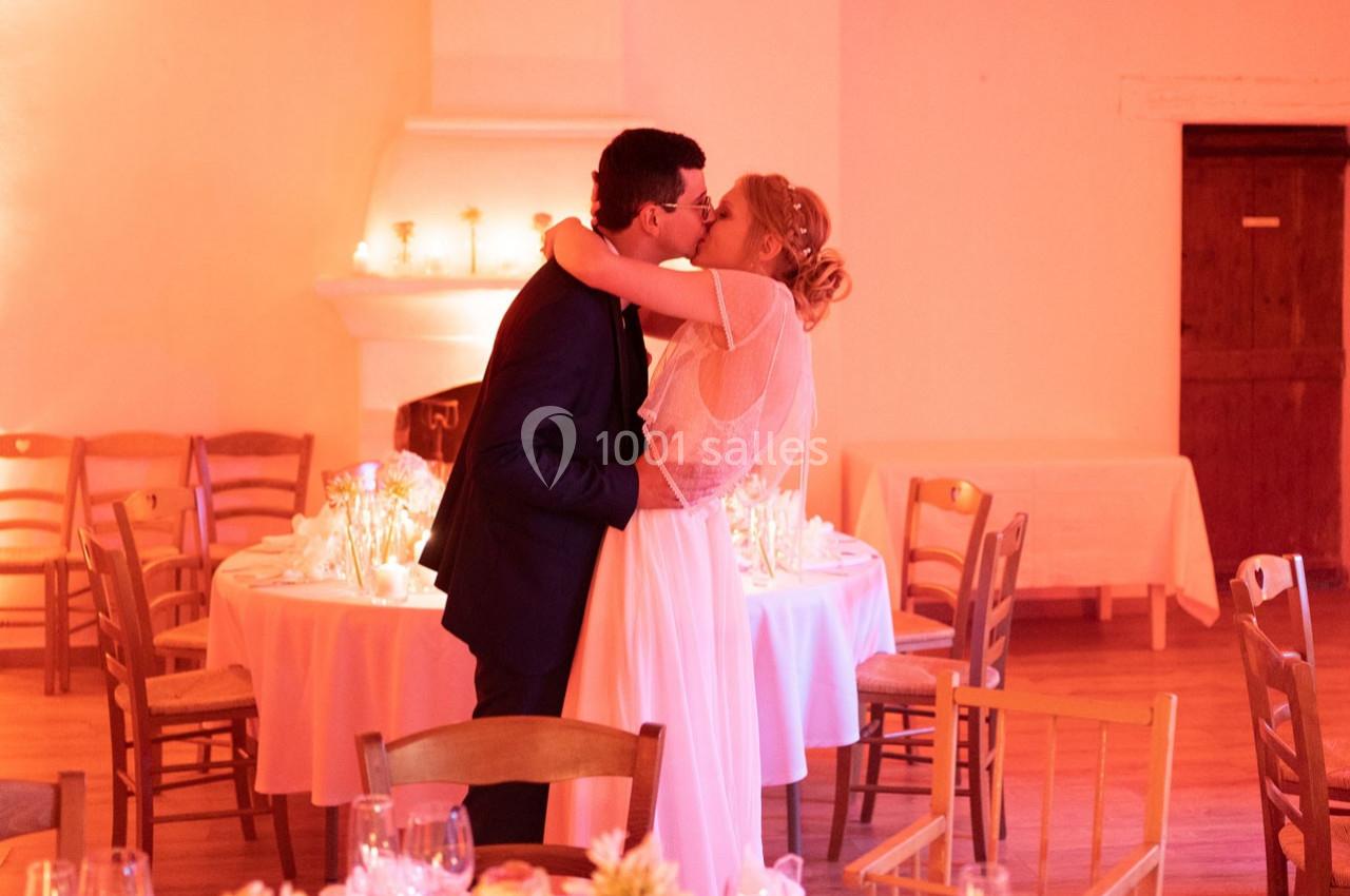 Un couple en tenue de mariage s'embrasse dans une salle décorée avec des tables et des bougies.