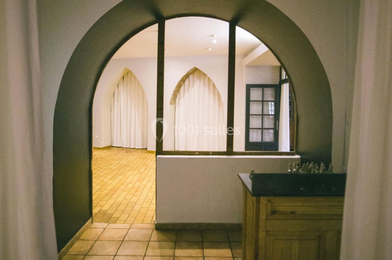 Vue d'un intérieur avec une arche, des rideaux blancs et un sol en carreaux de terre cuite.