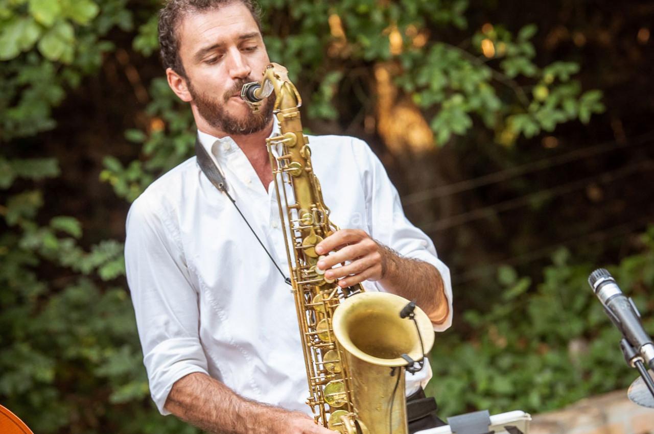Un homme joue du saxophone en plein air, entouré de verdure.