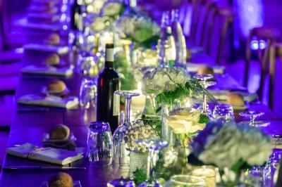 Salle de réception avec tables rondes dressées, nappes blanches, chaises en bois et décoration florale.