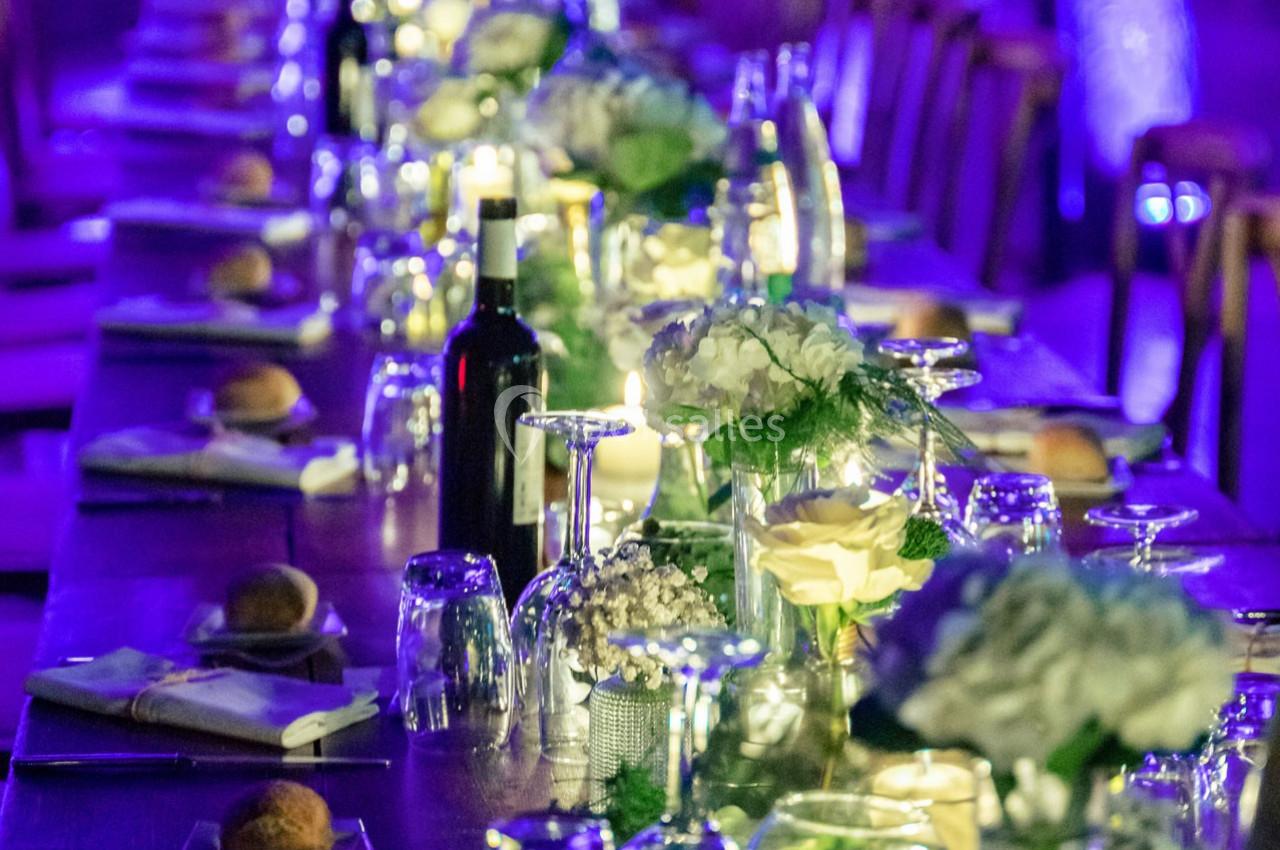 Table décorée pour un dîner, ornée de fleurs blanches, verres, bougies et une bouteille de vin, éclairage tamisé.