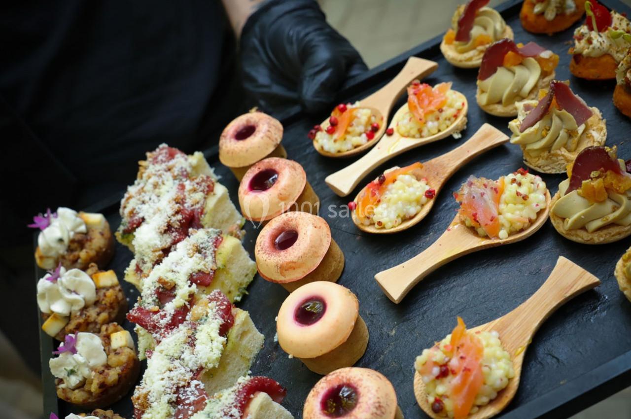 Plateau de bouchées apéritives variées comprenant canapés, cuillères garnies et petits gâteaux colorés.